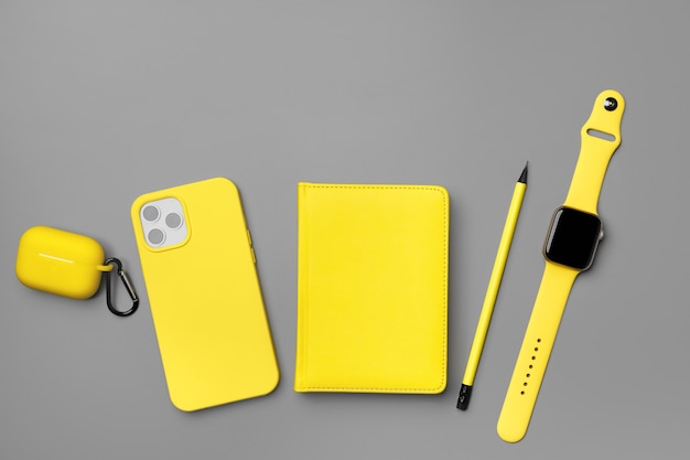 Bloco de notas amarelo com smartphone, smartwatch e fones de ouvido na vista superior cinza