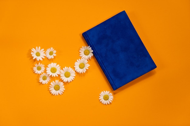 Bloco de notas azul marinho com lençóis brancos e margaridas brancas em fundo laranja de verão Planos para o verão para fazer a lista