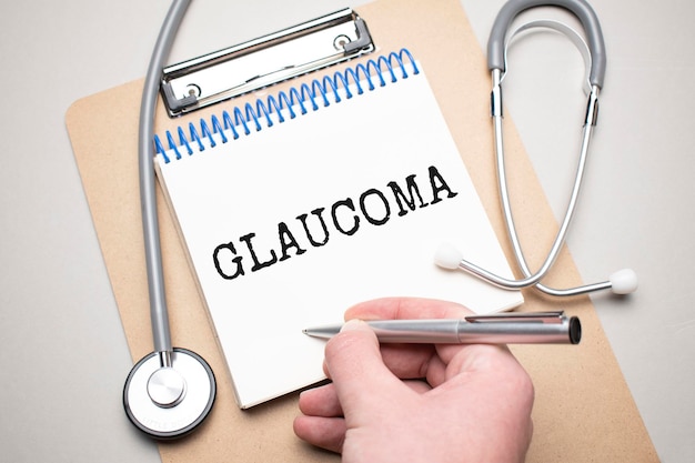 Bloco de notas branco com as palavras glaucoma e um estetoscópio sobre um fundo azul. Conceito médico