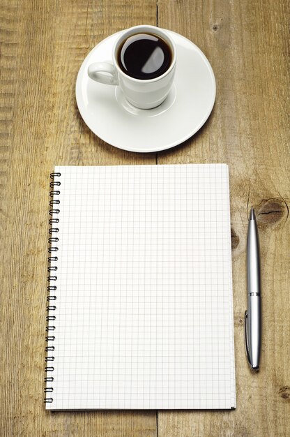 Bloco de notas, caneta e café em uma mesa de madeira