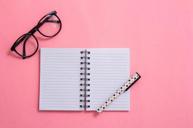 Bloco de notas, caneta e óculos em fundo rosa