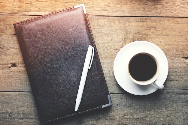 Bloco de notas, caneta e xícara de café preto na mesa de madeira