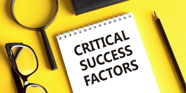 Bloco de notas com o texto fatores críticos de sucesso em um fundo amarelo com óculos uma lupa e um lápis conceito de negócio