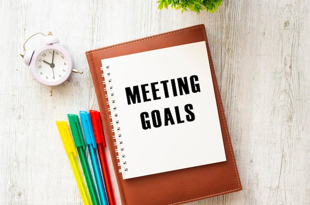 Bloco de notas com o texto MEETING GOALS em uma mesa de madeira Diário e canetas marrons