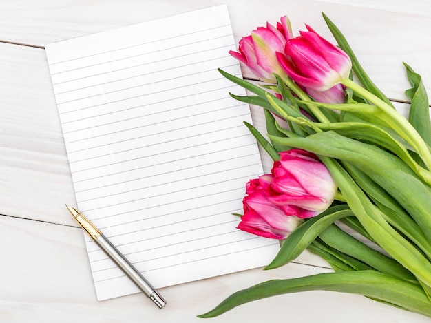 Bloco de notas em branco e buquê com tulipas na mesa de madeira Vista superior