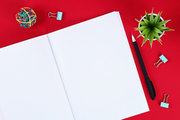 Bloco de notas em branco na mesa vermelha, planta, caneta.
