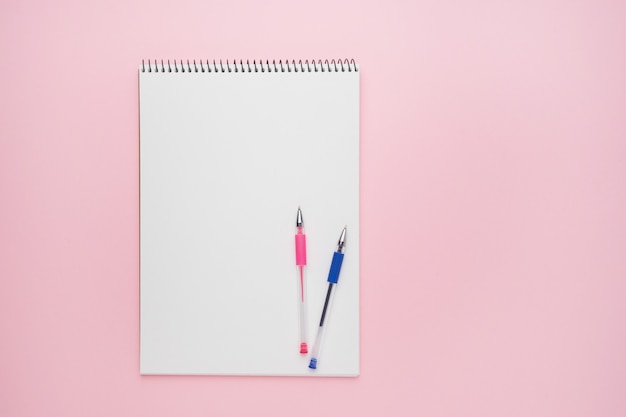 Bloco de notas em espiral com canetas como maquete para seu projeto. Caderno em pano de fundo rosa pastel. De volta ao conceito de escola. Copie o espaço