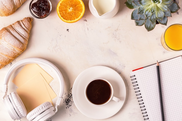 Bloco de notas, fones de ouvido, croissants e café na mesa branca.