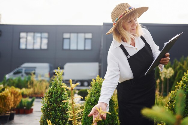 Bloco de notas nas mãos A mulher sênior está no jardim durante o dia Concepção de plantas e estações