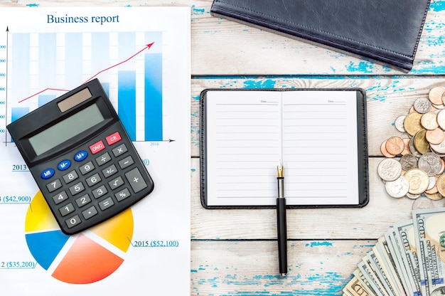 Bloco de notas no local de trabalho do escritório com dinheiro de calculadora de caneta e gráficos de negócios em cima da mesa