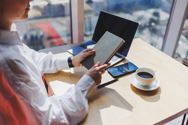 Bloco de notas para entradas em mãos femininas no fundo de um laptop closeup uma xícara de café em uma mesa de madeira Mesa do empresário Foco seletivo do processo de trabalho