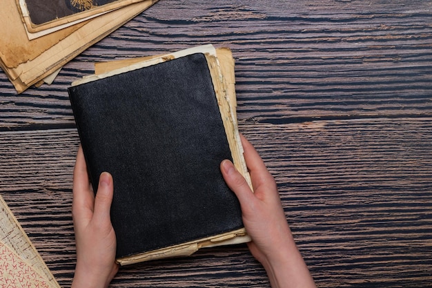 Foto bloco de notas preto vintage com folhas de papel velhas em ambas as mãos e espaço de cópia em fundo de madeira