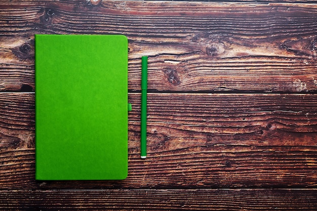 Bloco de notas verde com uma caneta com ponta de feltro em uma mesa de madeira marrom, vista superior.