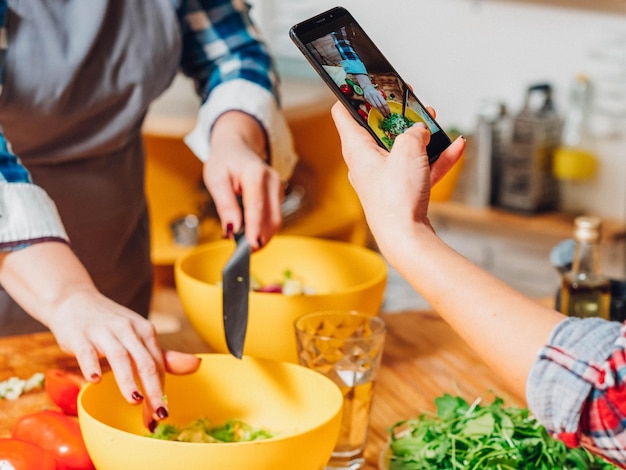 Foto blog de cocina dos mujeres haciendo ensalada cortando verduras tomando fotos de teléfonos inteligentes nutrición saludable estilo de vida vegano