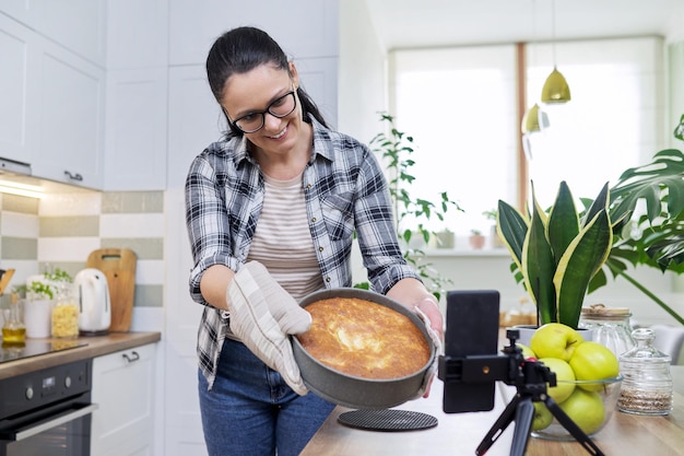 Blog de comida mujer cocinando tarta de manzana en casa grabando receta en smartphone