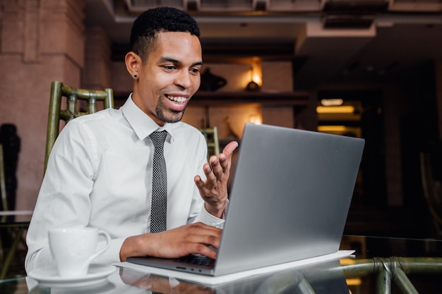 Blogger afroamericano expresa positivamente su computadora portátil, con una camisa blanca, interior