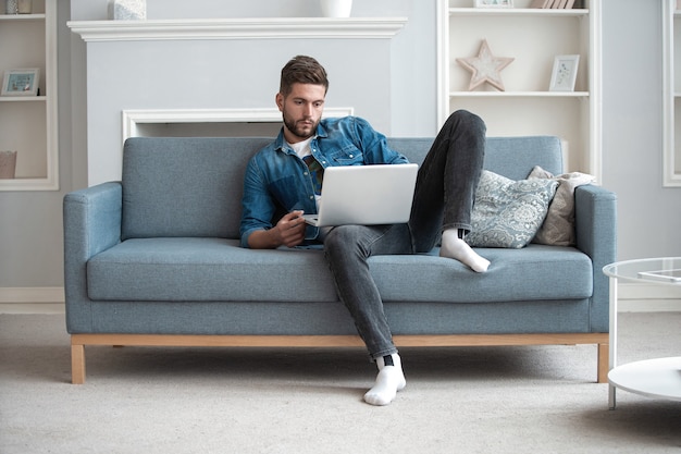 Blogger alegre. Diseñador de hombre moderno guapo que trabaja en la computadora portátil en línea, usando internet en casa