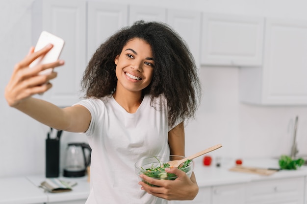 Blogger americano africano bonito que cozinha o jantar na cozinha, fluindo o vídeo. Conceito de estilo de vida saudável