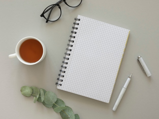 Blogger Arbeitsplatz flach lag Modell. Hipster's Glasses und geöffnetes Notizbuch mit leerem Blatt Papier, Tee und Eukalyptus.