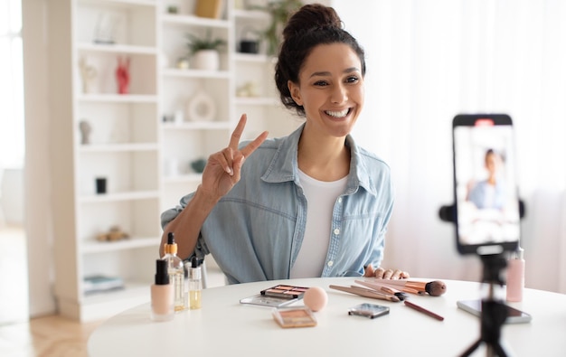 Blogger de belleza femenina haciendo un video que gesticula la victoria al teléfono celular en el interior