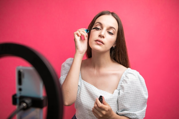 Blogger de belleza grabando tutorial de maquillaje sobre fondo rosa