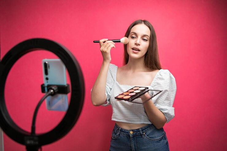 Blogger de belleza grabando tutorial de maquillaje sobre fondo rosa