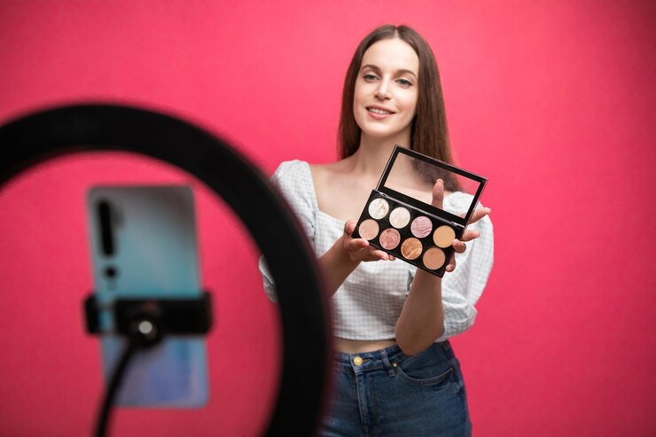 Foto blogger de belleza grabando tutorial de maquillaje sobre fondo rosa