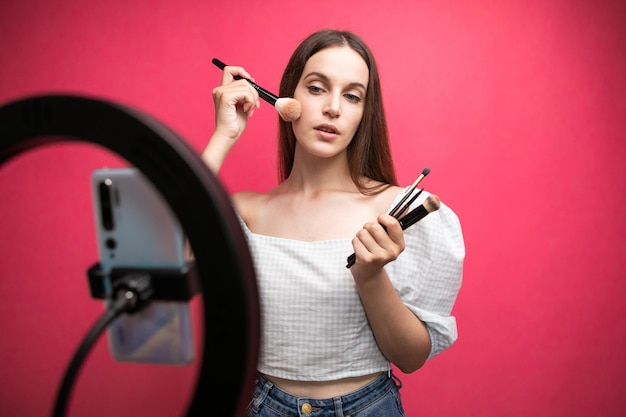 Blogger de belleza grabando tutorial de maquillaje sobre fondo rosa