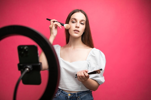 Foto blogger de belleza grabando tutorial de maquillaje sobre fondo rosa