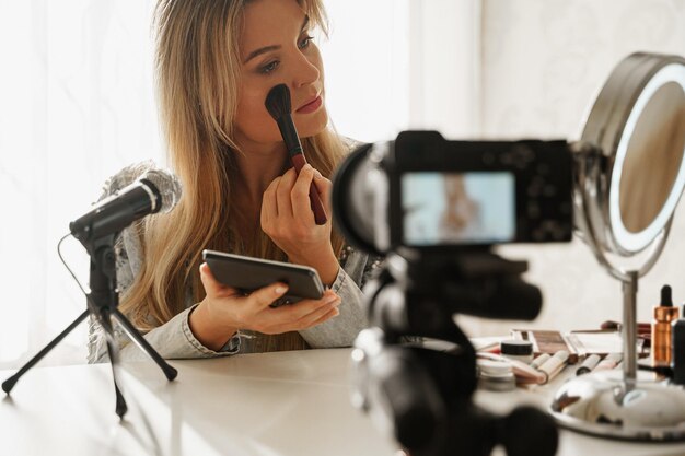 Blogger de belleza mujer aplicando polvo de rubor en su rostro durante la grabación de video para sus seguidores