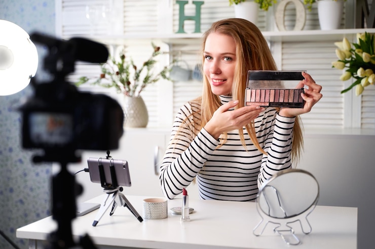 Foto blogger de belleza mujer filmando rutina de maquillaje diario tutorial cerca de la cámara en el trípode influencer chica transmisión en vivo revisión de productos cosméticos en el estudio en casa vlogger mujer mostrando la paleta de sombras para los ojos
