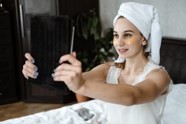 Foto blogger de belleza vlogger influencer mujer joven en pijama toalla en la cabeza y con cosméticos