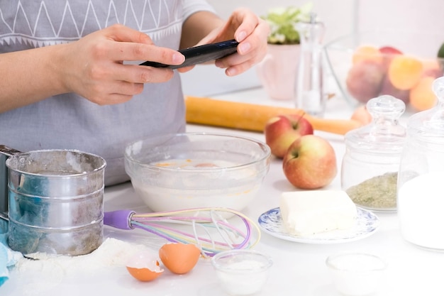 El blogger de cocina está cocinando en la cocina en un día soleado y está haciendo una foto en el teléfono inteligente del proceso de cocción Mujer bonita joven cocinando en la cocina