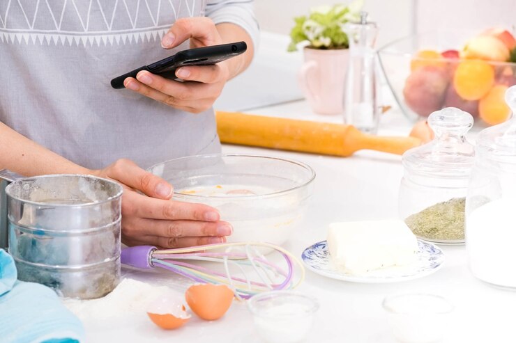 Foto el blogger de cocina está cocinando en la cocina en un día soleado y está haciendo una foto en el teléfono inteligente del proceso de cocción mujer bonita joven cocinando en la cocina