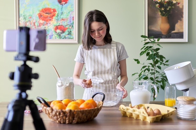 Blogger de comida adolescente chica cocinando panqueques de naranja en casa en la cocina. Ingredientes productos harina, naranjas, leche, azúcar, huevos rotos. Pasatiempos de cocina canal de seguidores para niñas, adolescentes y niños