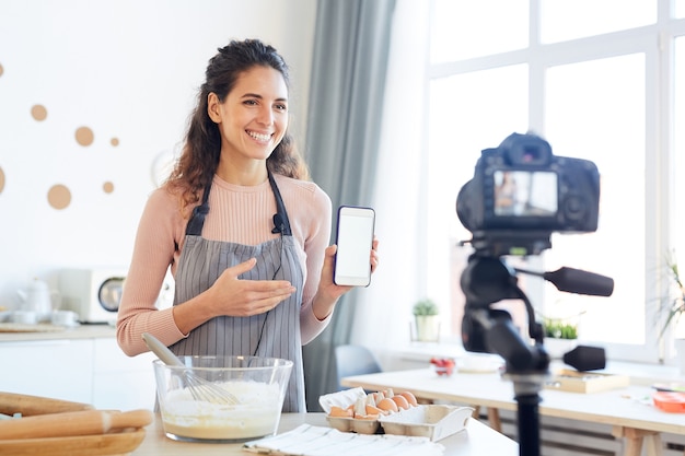 Blogger de comida femenina joven que demuestra la nueva aplicación de teléfono móvil en la cámara