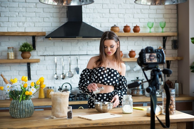 Blogger de comida de niña bastante joven en vestido de lunares trabajando en un nuevo video y explicando cómo cocinar un plato.