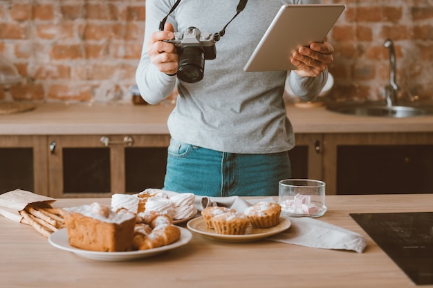 Blogger de comida. Pasatiempo y estilo de vida. Hombre con tableta y cámara. Surtido de tortas y pasteles alrededor.