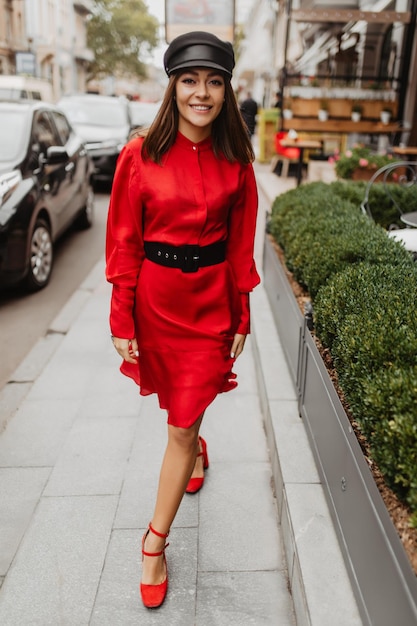 Blogger con estilo en traje rojo y negro con accesorios geniales se mueve con confianza Toma completa de mujer parisina sonriente