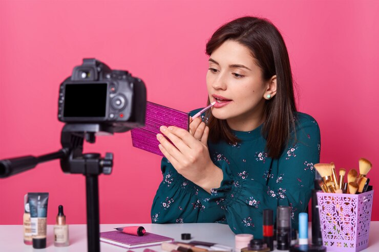 Foto blogger femenina haciendo video para blog de belleza, sentada en una mesa blanca contra rosa