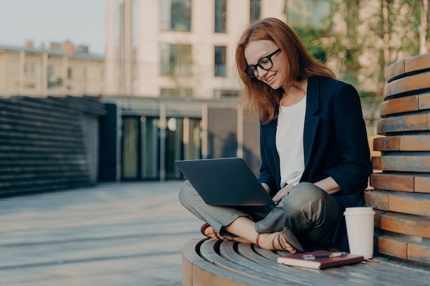 Blogger femenino positivo o texto de tipo freelancer de publicación en una computadora portátil