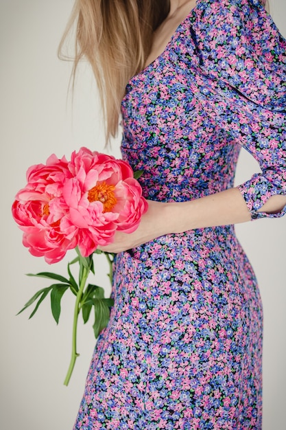 Blogger girl está sosteniendo un ramo de poonies rojos vestida con un vestido morado con un estampado de flores sobre un fondo blanco en la sala de diseño moderno