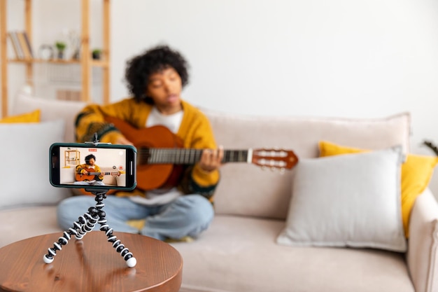 Blogger guitarrista afro-americana blogueira tocando violão conversando com webcam gravando vlog Mulher influenciadora de mídia social transmitindo em casa dentro de casa Tutorial de transmissão do criador de conteúdo musical