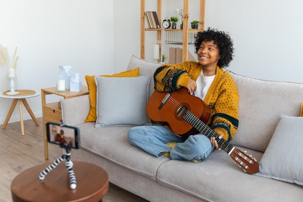 Blogger guitarrista bloguera afroamericana tocando guitarra hablando con cámara web grabando vlog soci