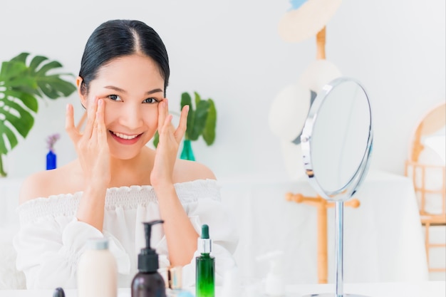 Blogger hermosa mujer asiática está mostrando cómo maquillarse y usar cosméticos. Frente al espejo y la cámara grabando video vlog en vivo en casa.Cuidado de la piel para el concepto de rostro saludable.