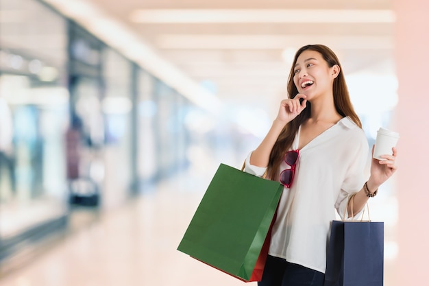 Blogger de hermosas mujeres asiáticas de compras y mano apuntando con una bolsa de compras en el centro comercial borroso