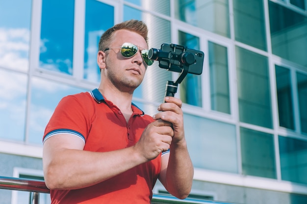 Blogger in der Stadt nimmt Videos auf einem Smartphone mit einem manuellen Kamerastabilisator auf.