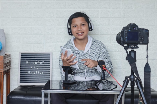 Blogger infantil asiático sosteniendo una tableta digital mientras hace un blog de video. Niño influyente en línea social med