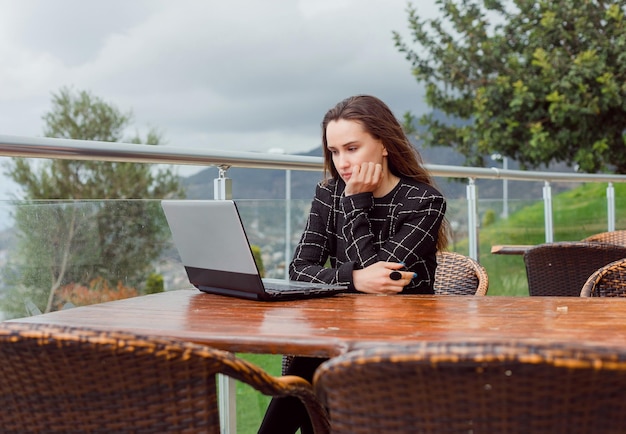 Blogger-Mädchen schaut auf ihren Laptop-Bildschirm, indem sie die Hand unter das Kinn auf den Hintergrund der Naturansicht legt