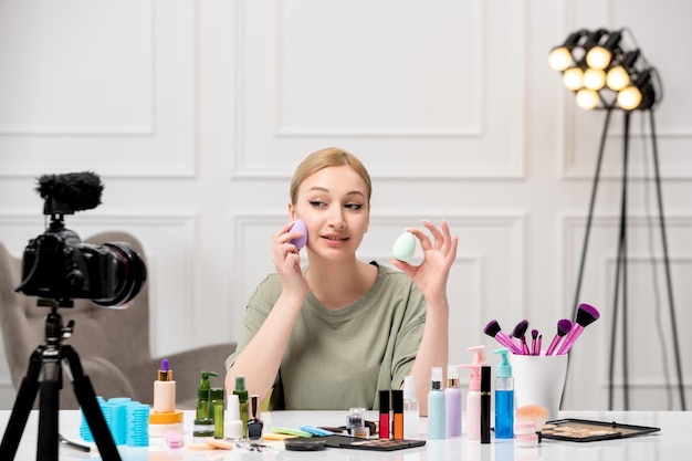 Blogger de maquillaje creando tutorial de maquillaje en la cámara joven linda linda chica con dos esponjas suaves